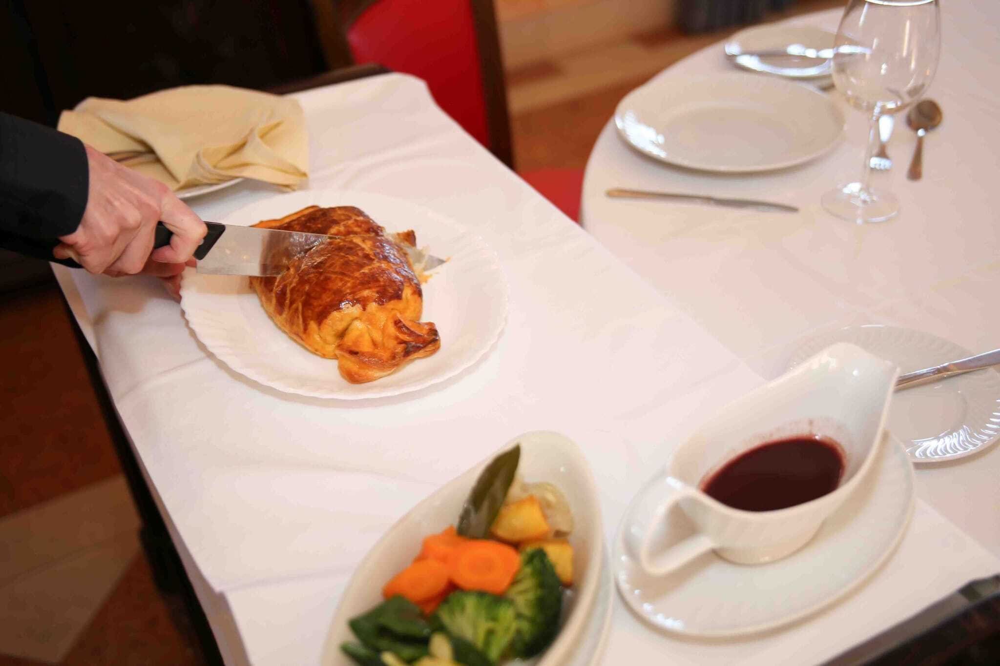 A dining table with a roasted chicken, a bowl of vegetables, and a cup of red sauce.