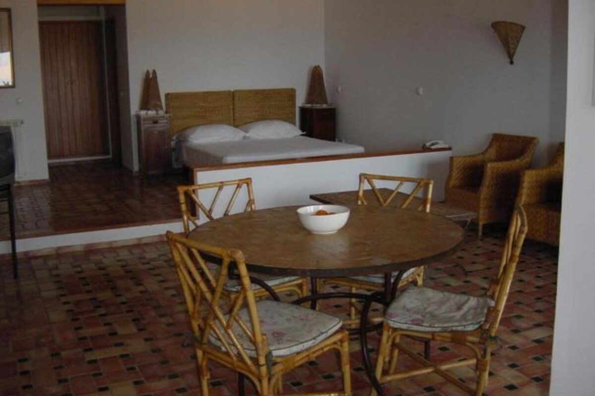 A room with a bed, a dining table with chairs, and a small kitchen area.