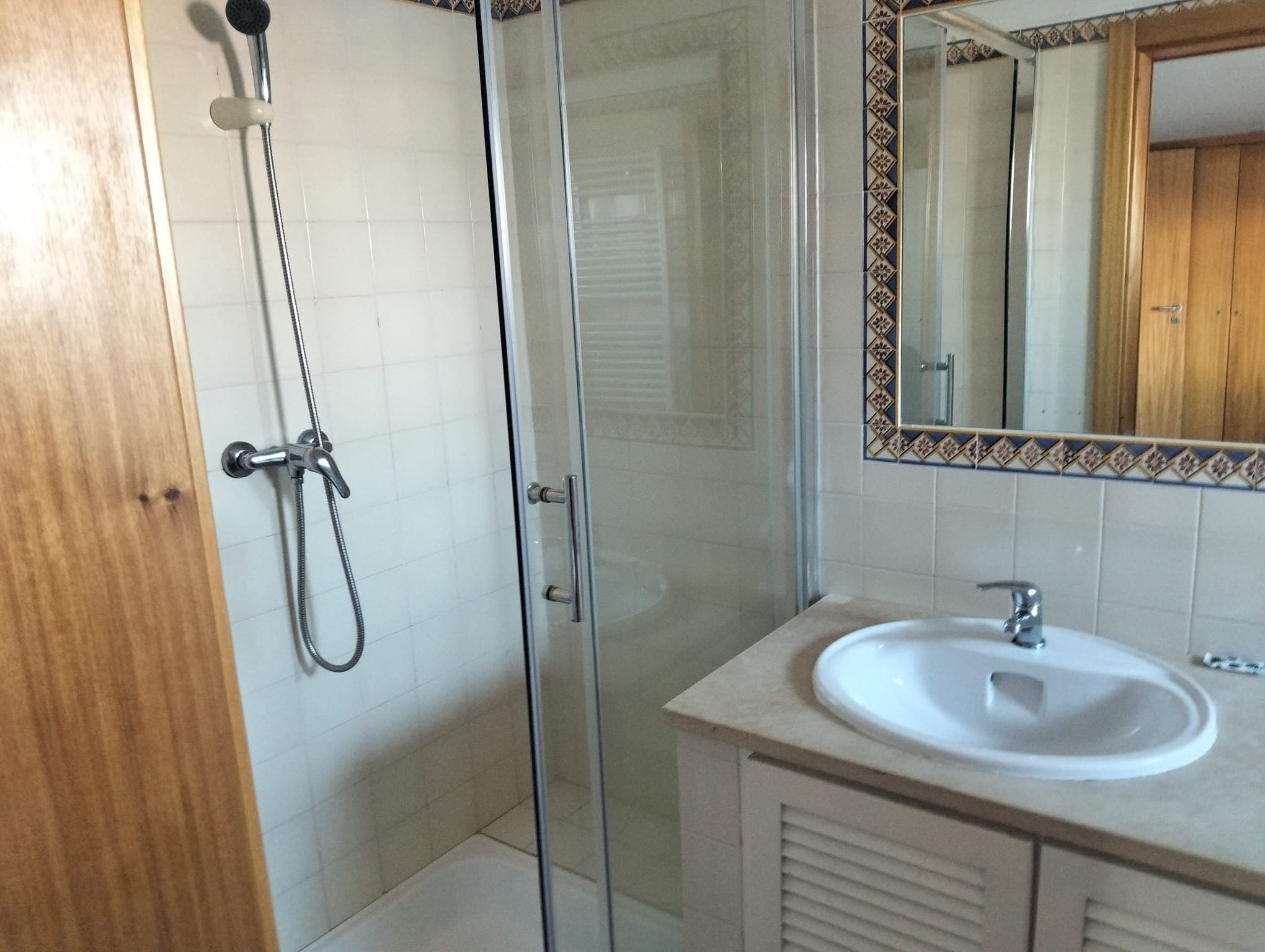 Un baño con cabina de ducha de vidrio, lavamanos y espejo con detalle decorativo.