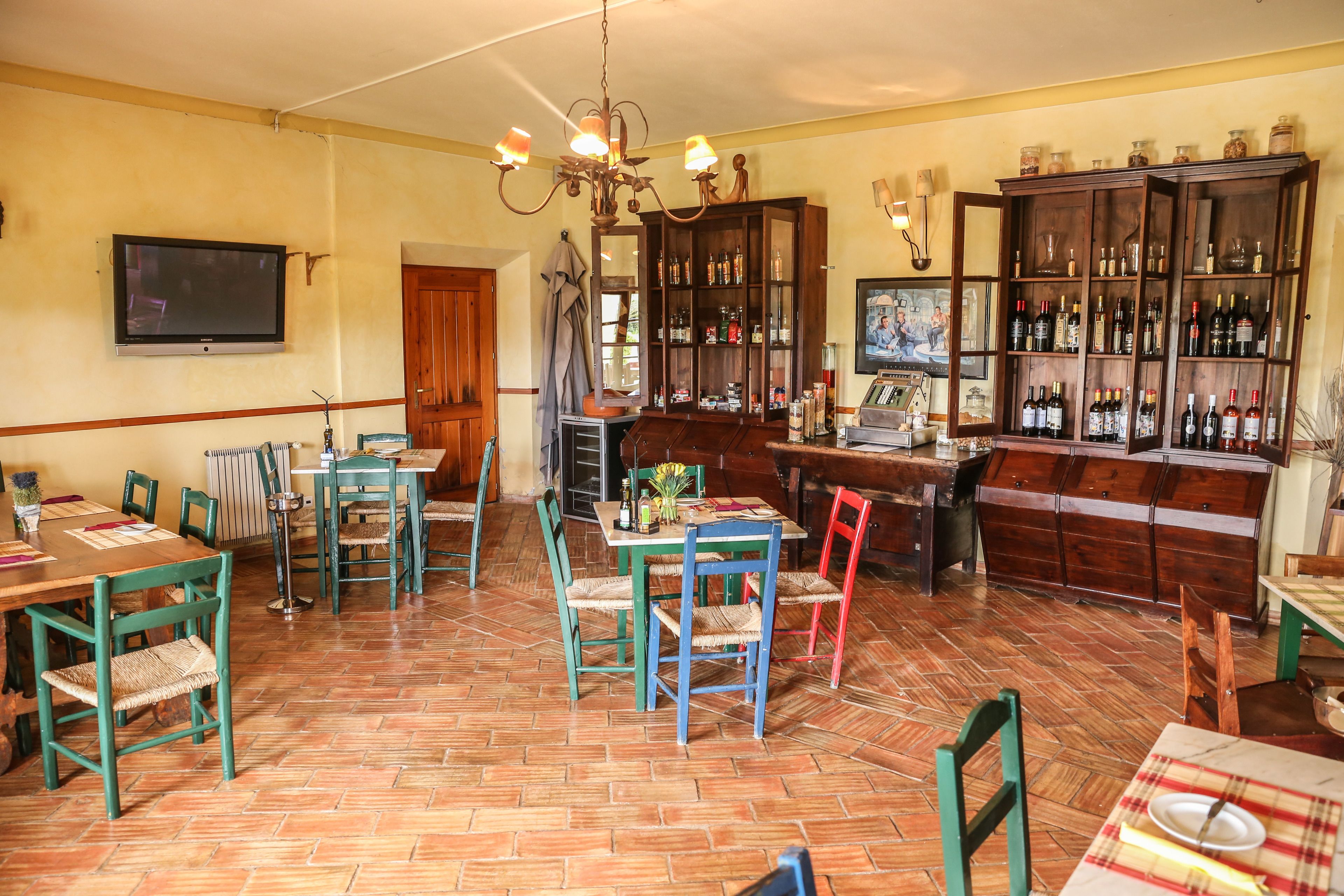 A dining area with a wooden table, chairs, a chandelier, and a bar area with shelves of bottles.