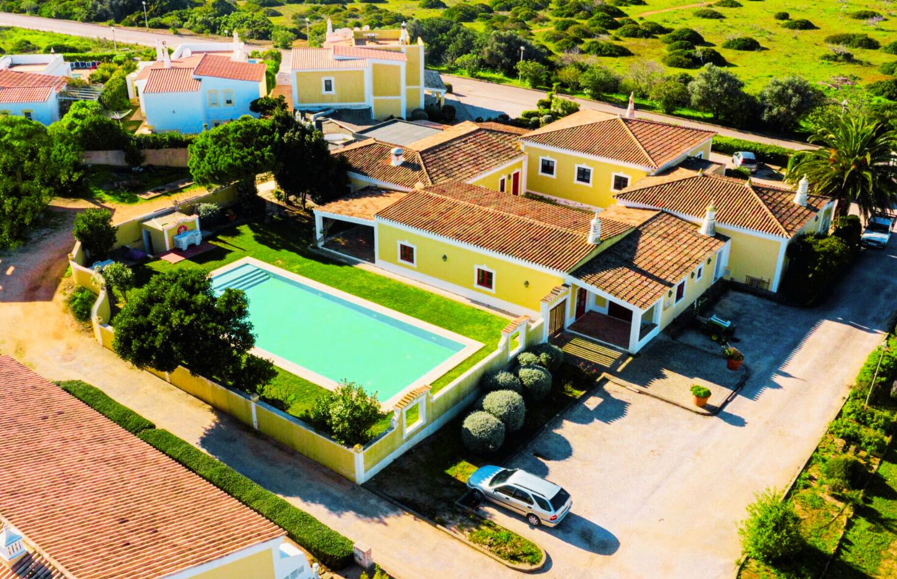A residential area with a swimming pool, multiple houses, and a parked car.