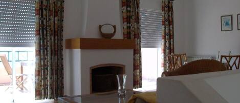 A room with a fireplace, curtains, a table, and a bed.