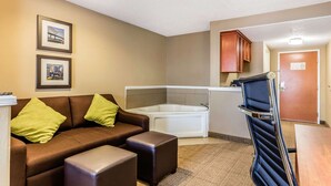 Habitación de hotel con un sofá de cuero marrón, dos almohadas verdes, una bañera blanca y una puerta de madera.