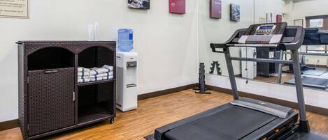 A fitness room with a treadmill, a water dispenser, and a storage unit with towels.