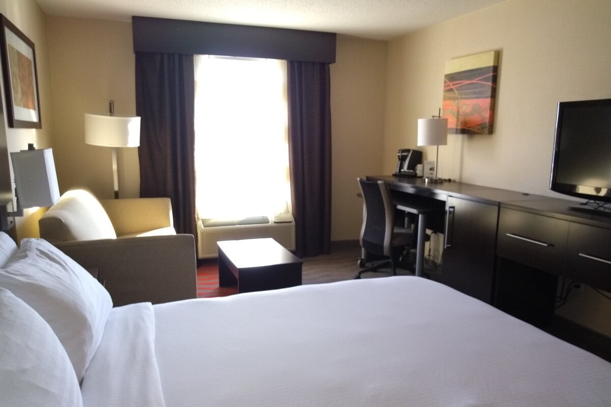 A hotel room with a bed, a desk, a chair, a TV, and a window with curtains.