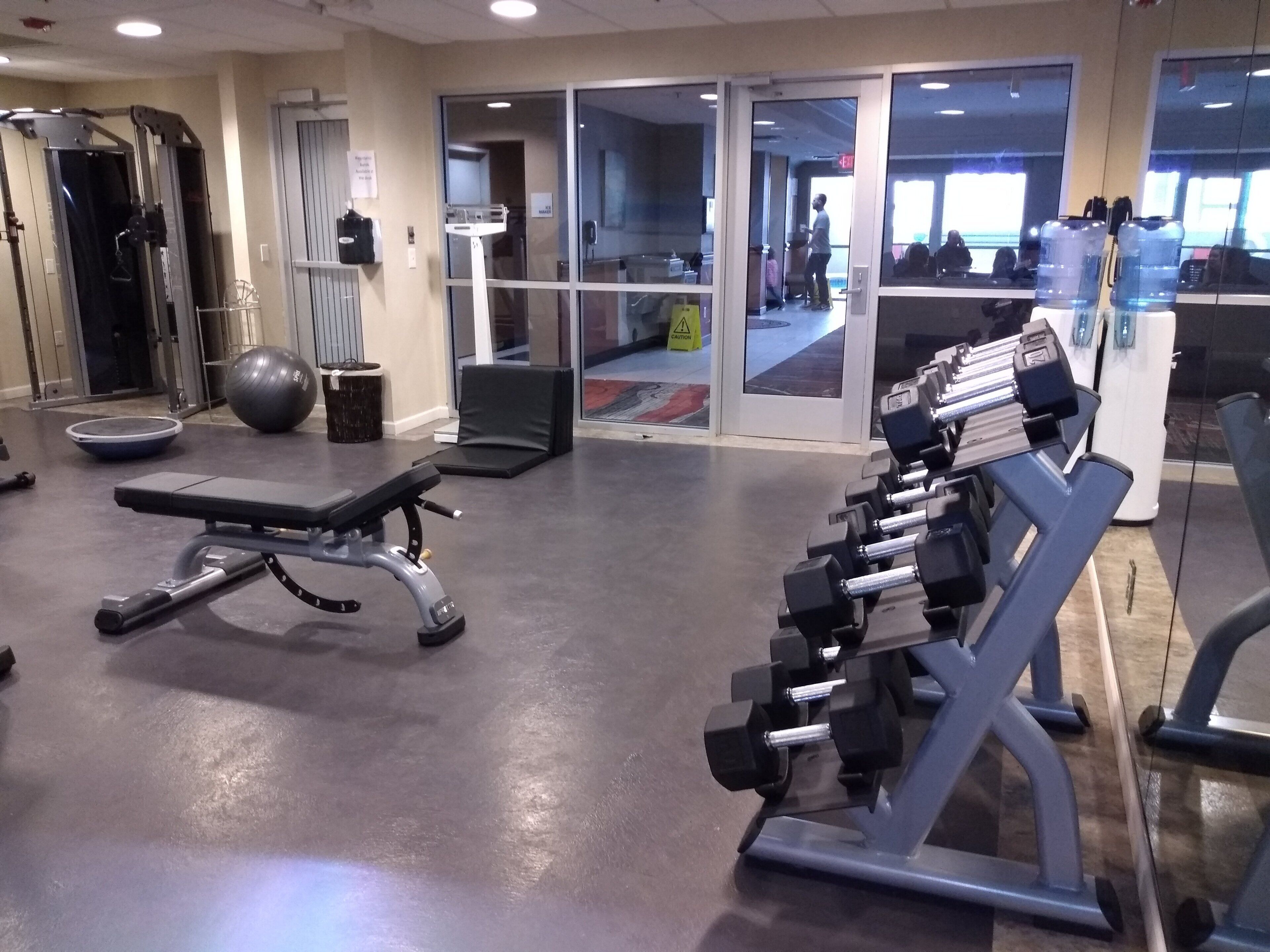 Un gimnasio con equipo de ejercicio, una banca y un espejo grande.