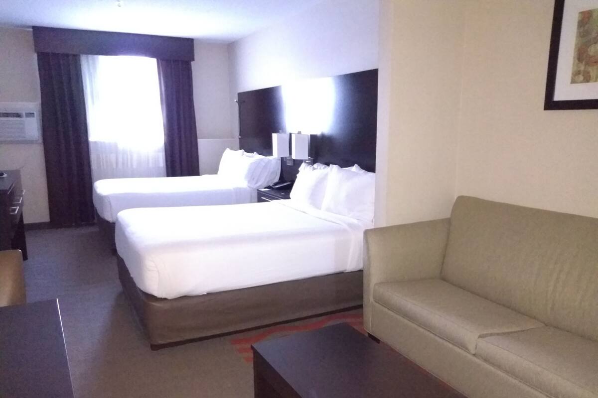 A hotel room with two single beds, a sofa, a desk, and a TV.