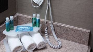 Un sèche-cheveux fixé au mur, une prise de courant, un interrupteur et un porte-serviettes avec des serviettes et des articles de toilette.