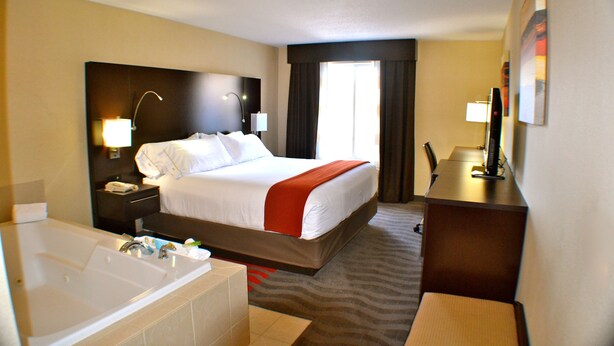 Une chambre d’hôtel avec un grand lit, une salle de bain séparée avec une baignoire, un bureau et une chaise.