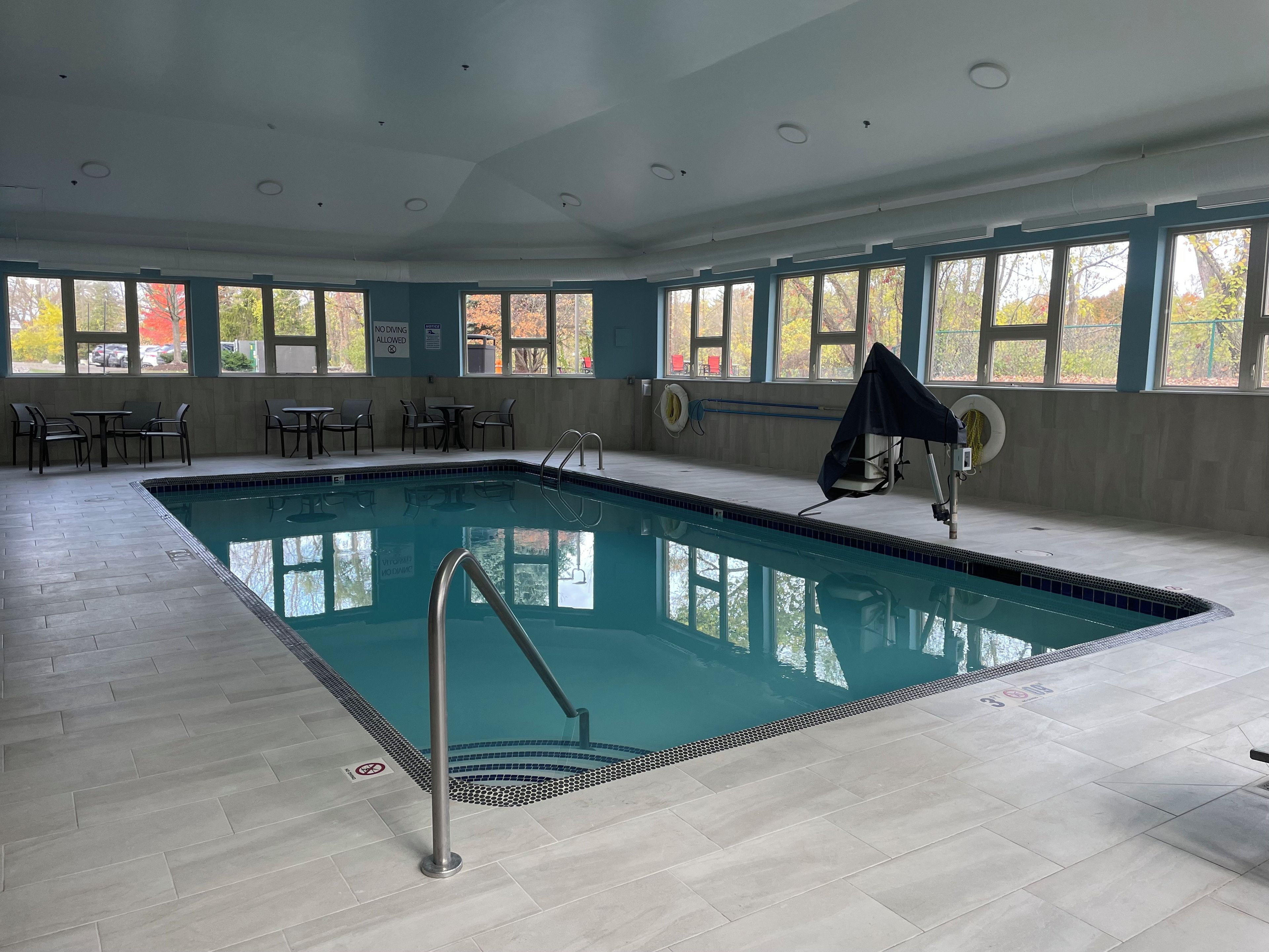An indoor swimming pool with clear blue water, surrounded by tiled flooring and equipped with a pool ladder.