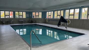 An indoor swimming pool with clear blue water, surrounded by tiled flooring and equipped with a pool ladder.