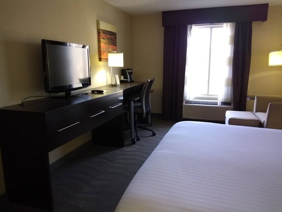 A hotel room with a bed, a desk with a TV, a chair, a lamp, and a window with curtains.