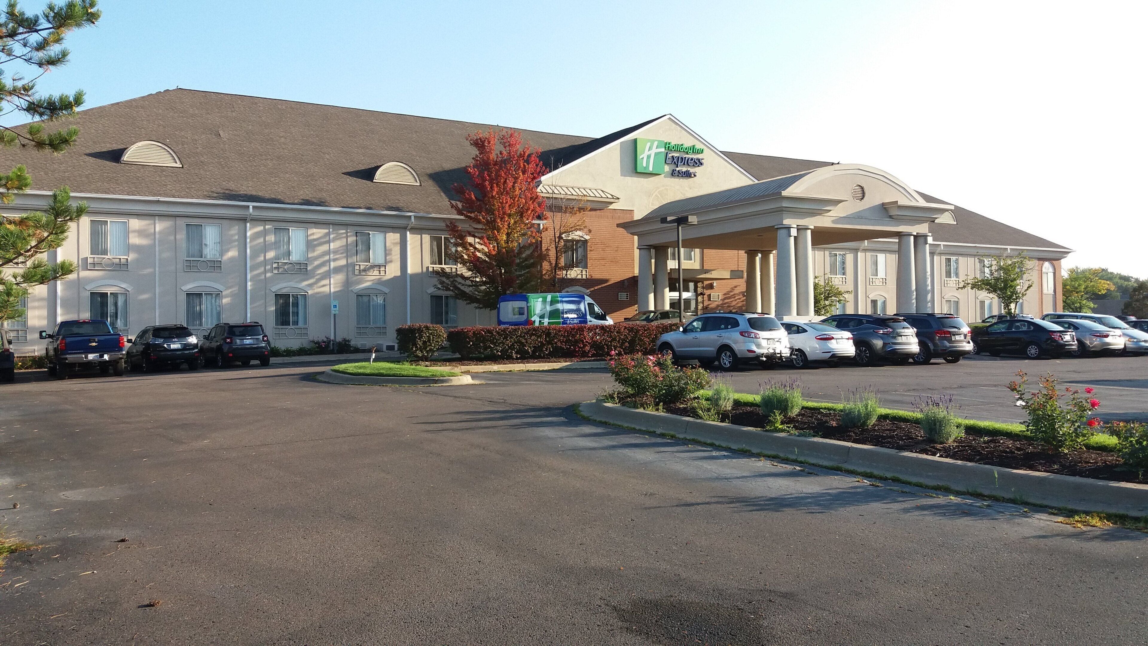 Un hôtel Holiday Inn Express doté d’un parking, où se trouvent plusieurs voitures garées et un camion de livraison.