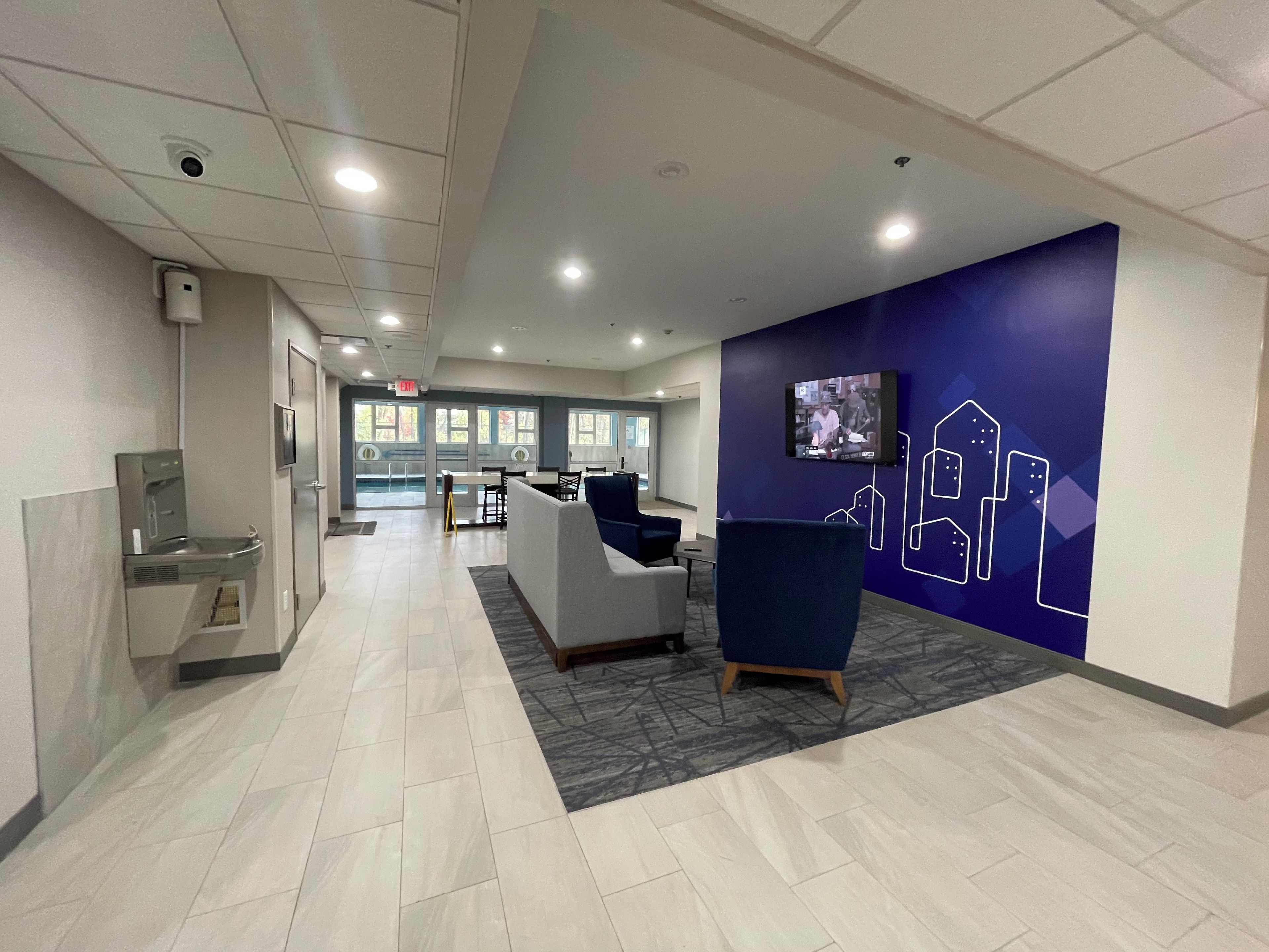 A modern lobby with a reception desk, seating area, and a TV screen displaying a program.