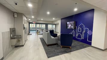 A modern lobby with a reception desk, seating area, and a TV screen displaying a program.