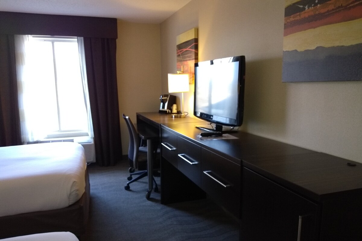 A hotel room with a bed, a desk with a computer, a chair, and a lamp.