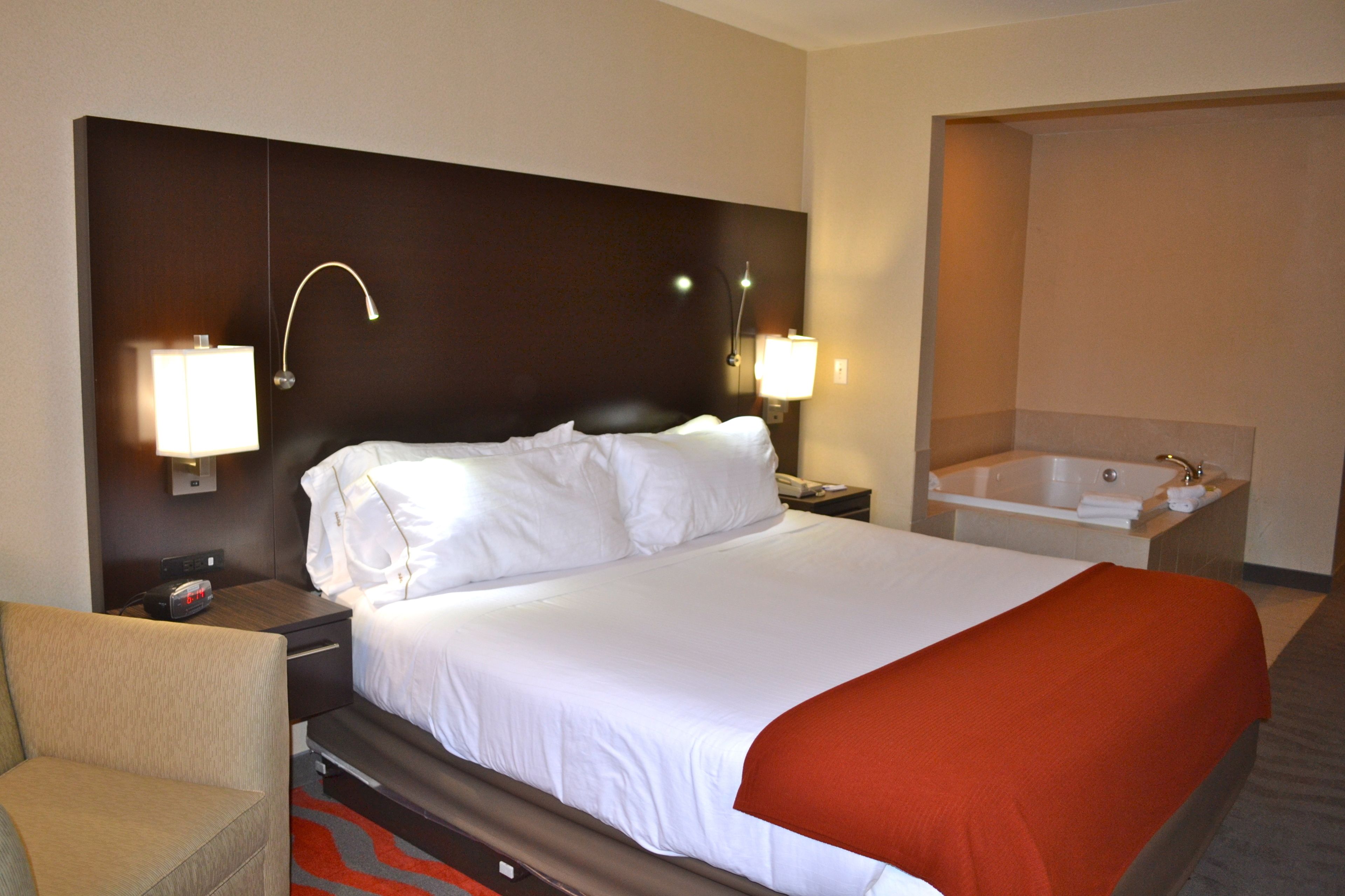 A hotel room with a large bed, two bedside lamps, a nightstand, a chair, and a separate bathroom with a bathtub.