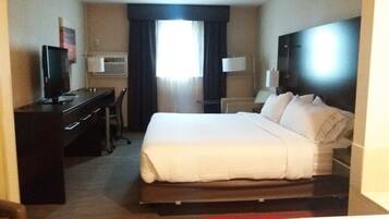 Una habitación de hotel con cama, escritorio, silla, televisor y ventana con cortinas.