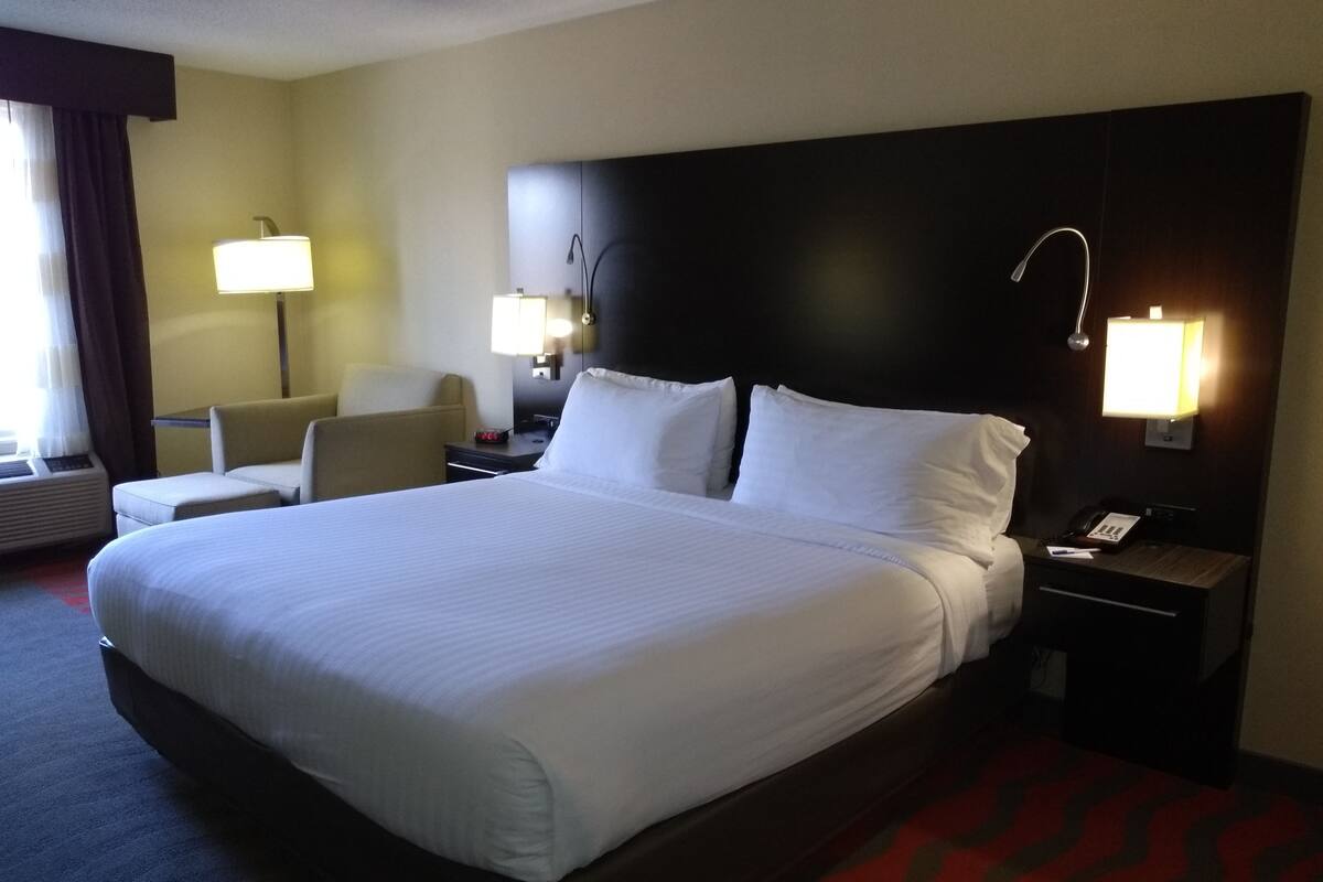A hotel room with a large bed, two bedside tables, a chair, a desk, and two wall-mounted lamps.