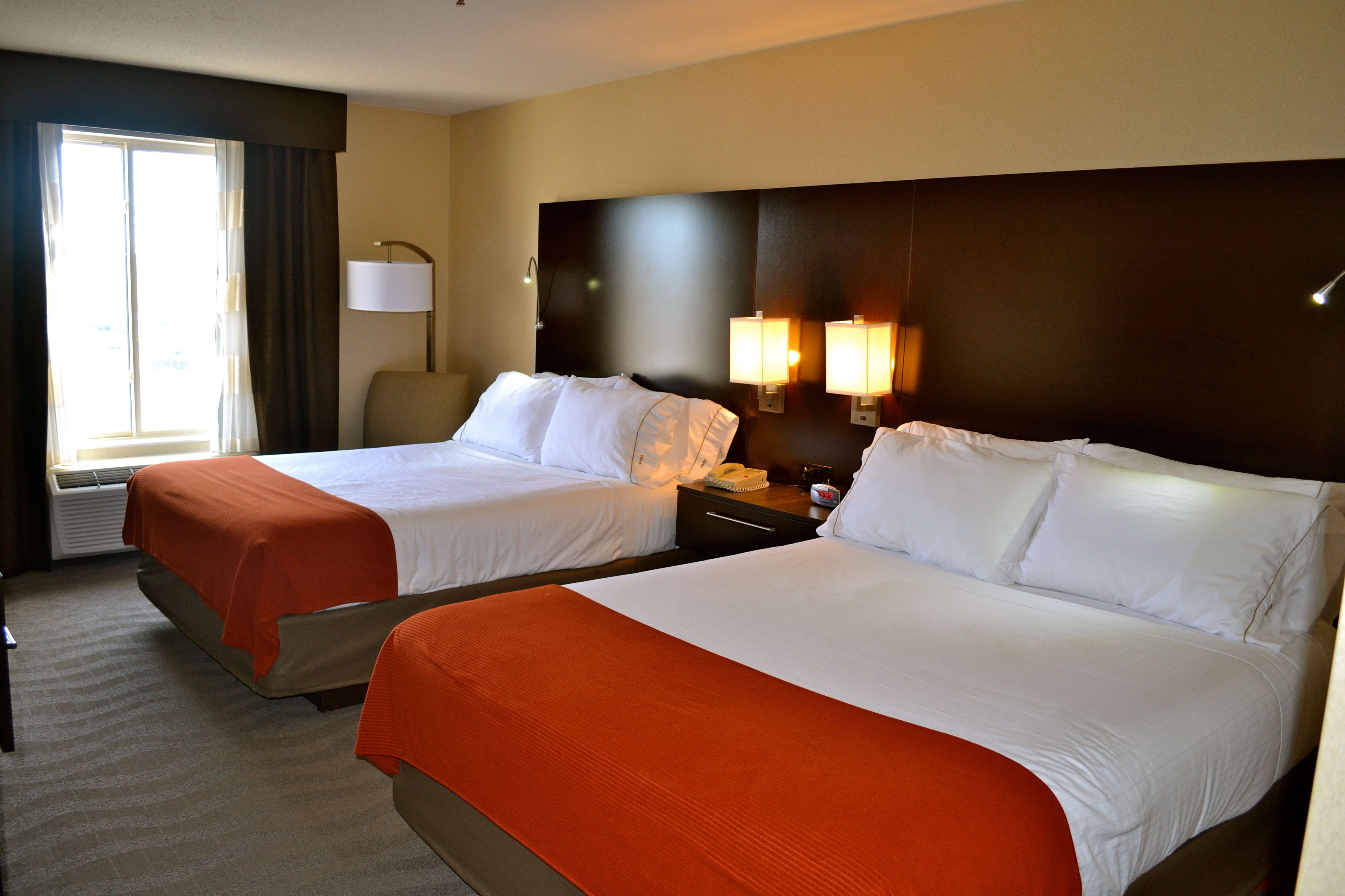 A hotel room with two beds, a desk, a chair, a lamp, and a window with curtains.