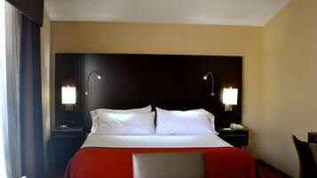 Una habitación de hotel con cama, lámparas de noche, un escritorio y una silla.