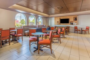 A restaurant with high tables and booths, large windows, and a flat-screen TV on the wall.