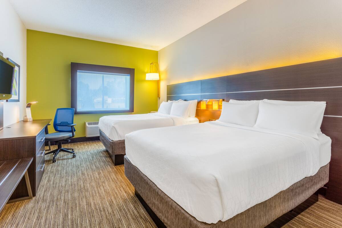 A hotel room with two beds, a desk, a chair, and a window with blinds.