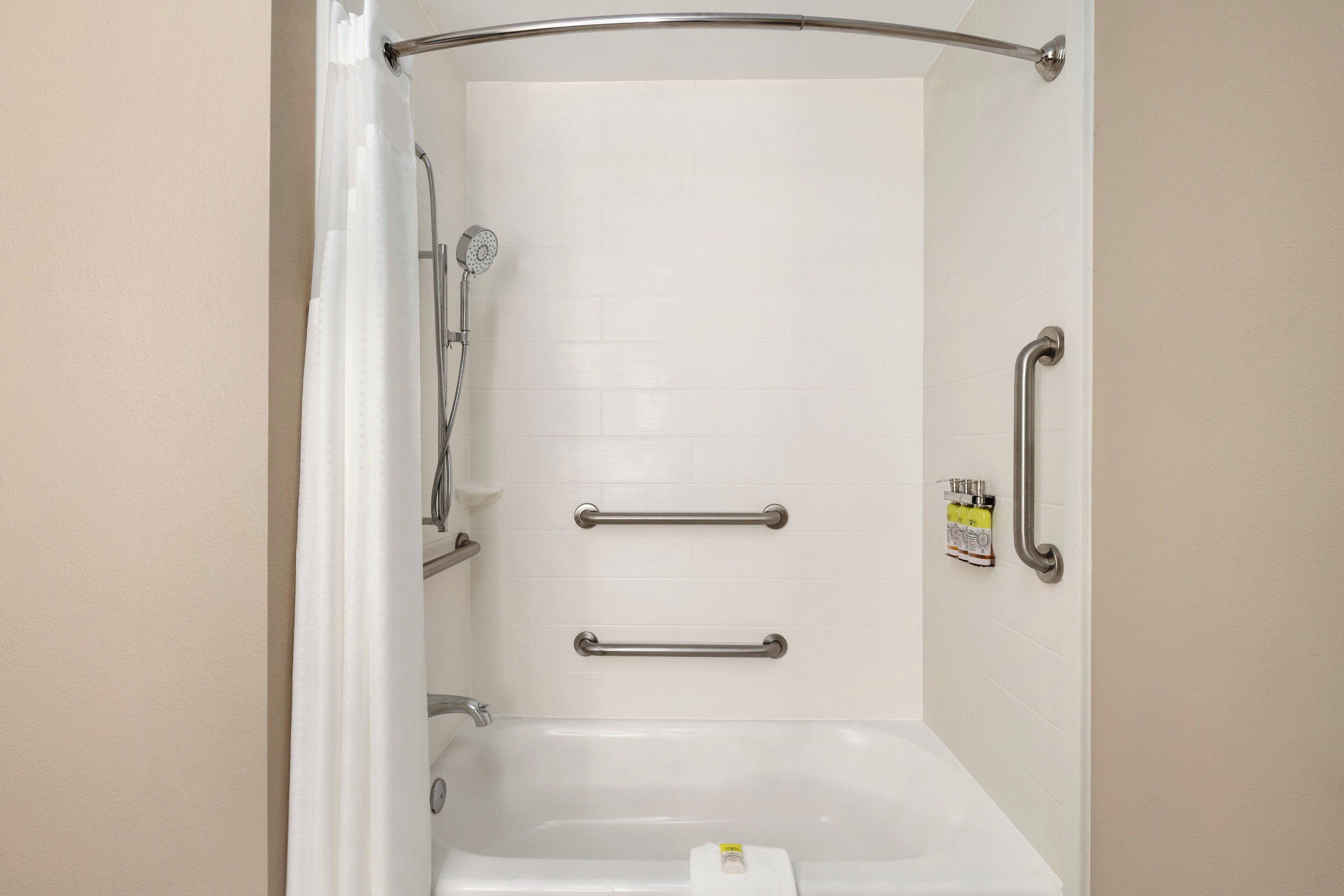 Une salle de bain équipée d’une baignoire, de barres d’appui et d’un pommeau de douche.