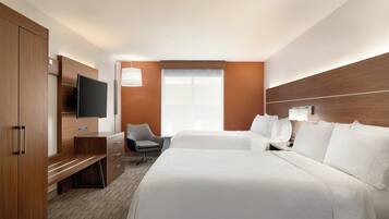A hotel room with a large bed, a desk with a flat-screen TV, a chair, and a window with blinds.
