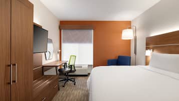 A hotel room with a bed, a desk with a chair, a TV, and a window with blinds.