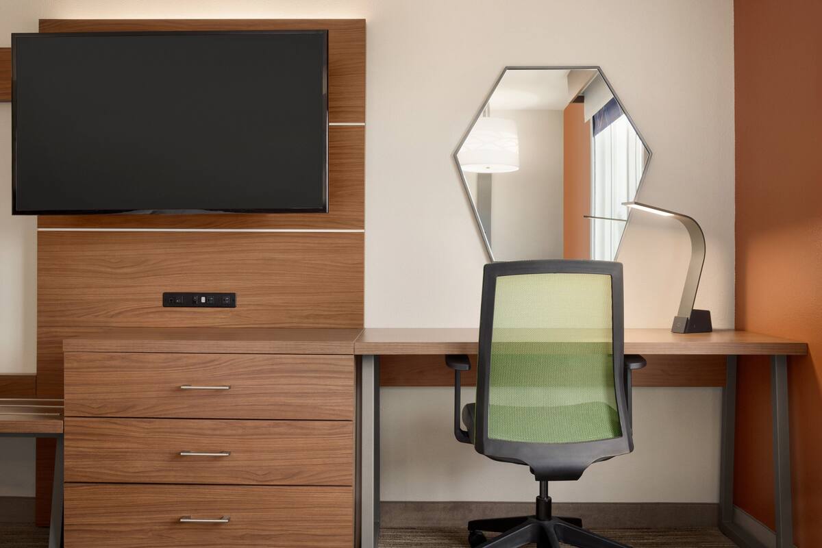 A modern office desk with a flat-screen TV, a mirror, and a chair.