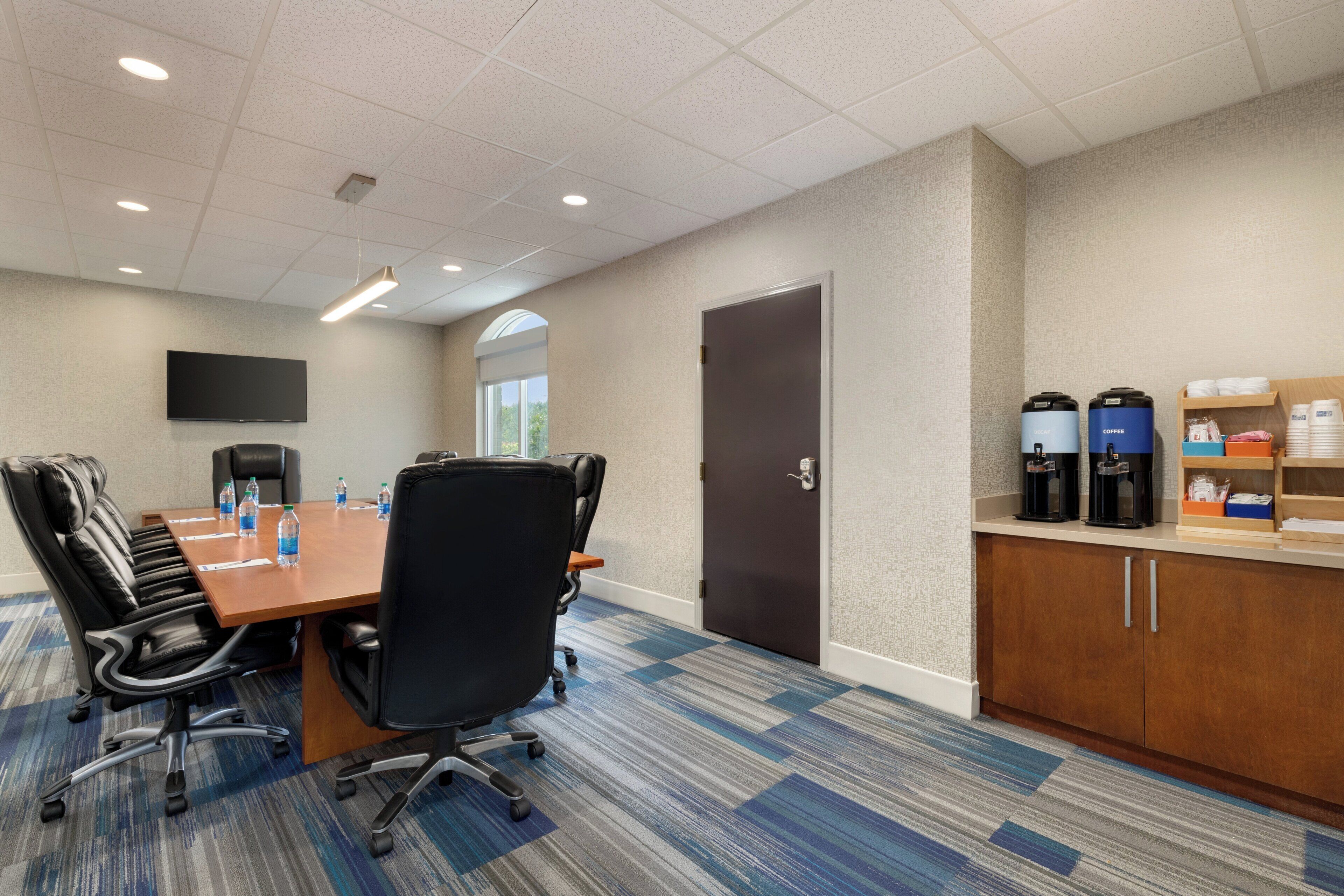 A conference room with a long table, chairs, a coffee station, and a door.
