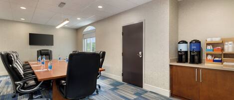 A conference room with a long table, chairs, a coffee station, and a door.