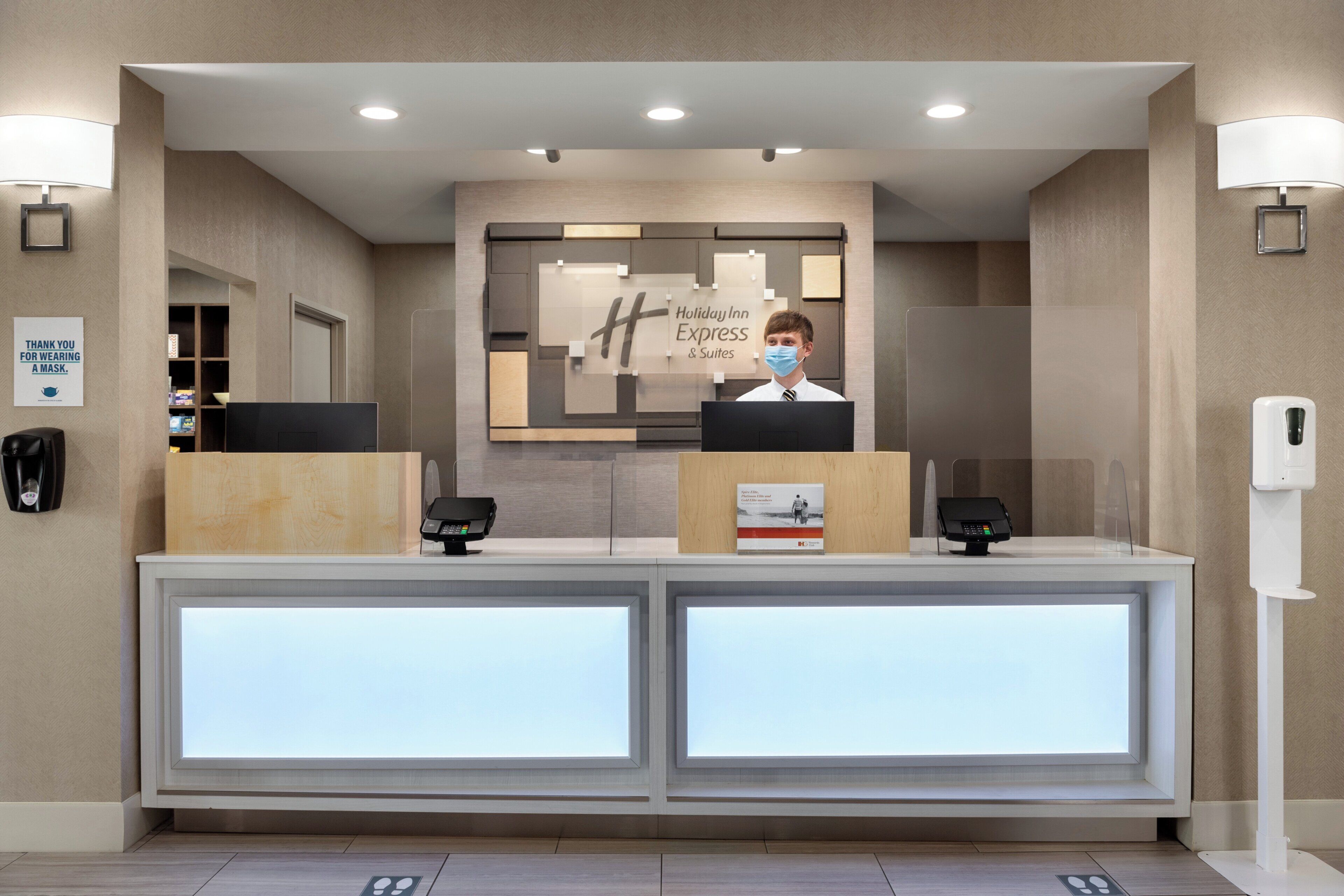A hotel reception desk with a digital display, a phone, and a sign thanking guests for wearing masks.