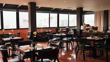 A restaurant with multiple tables and chairs, large windows with a city view, and a polished floor.