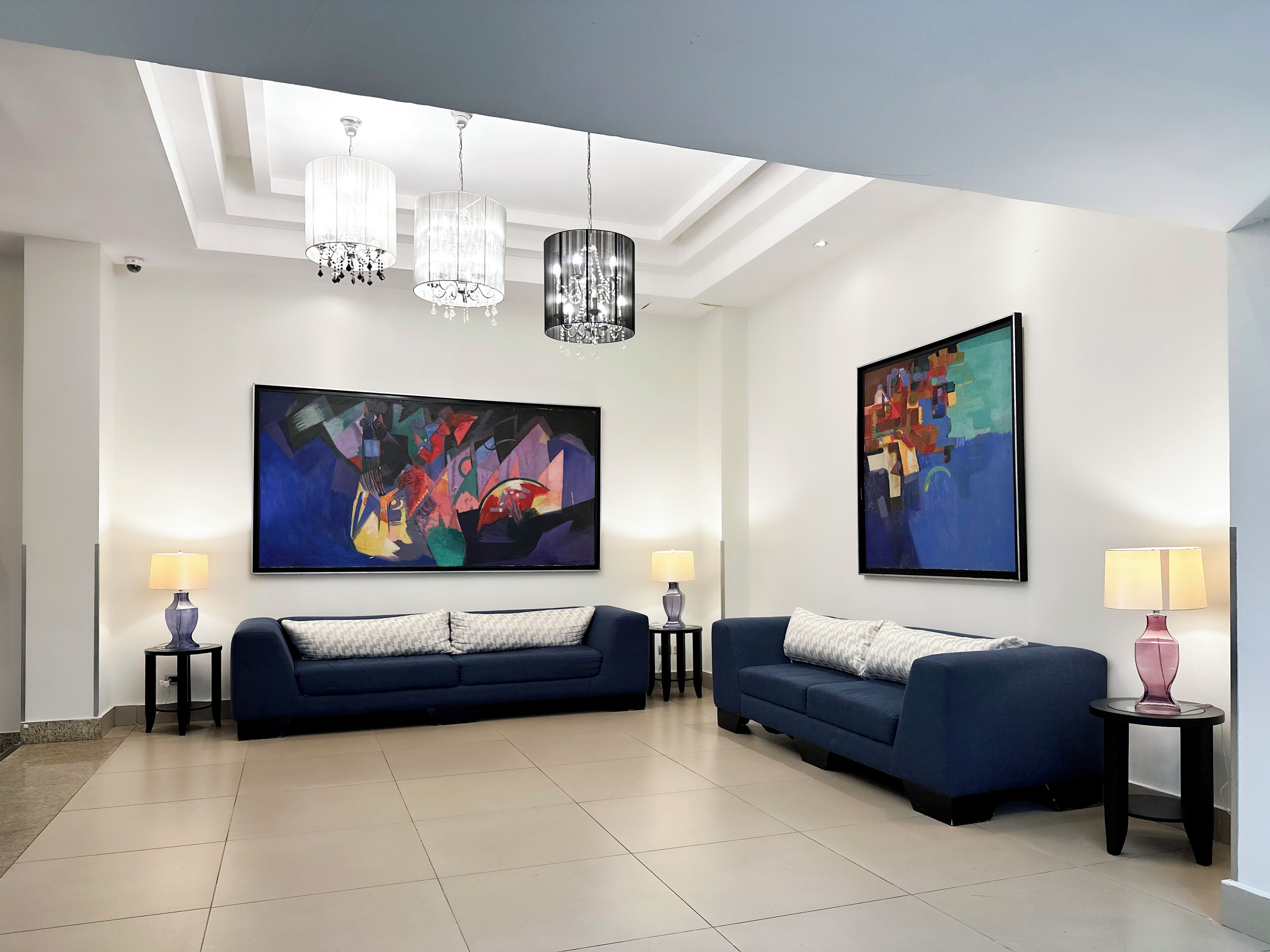 Un salon moderne avec deux canapés, un lustre et des tableaux abstraits accrochés aux murs.