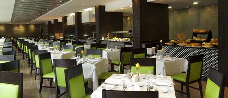 A restaurant with multiple tables set for dining, green chairs, and a buffet area in the background.
