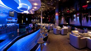 Un'area bar moderna con un bancone curvo, sgabelli da bar e un salotto con tavoli e sedie rotonde.