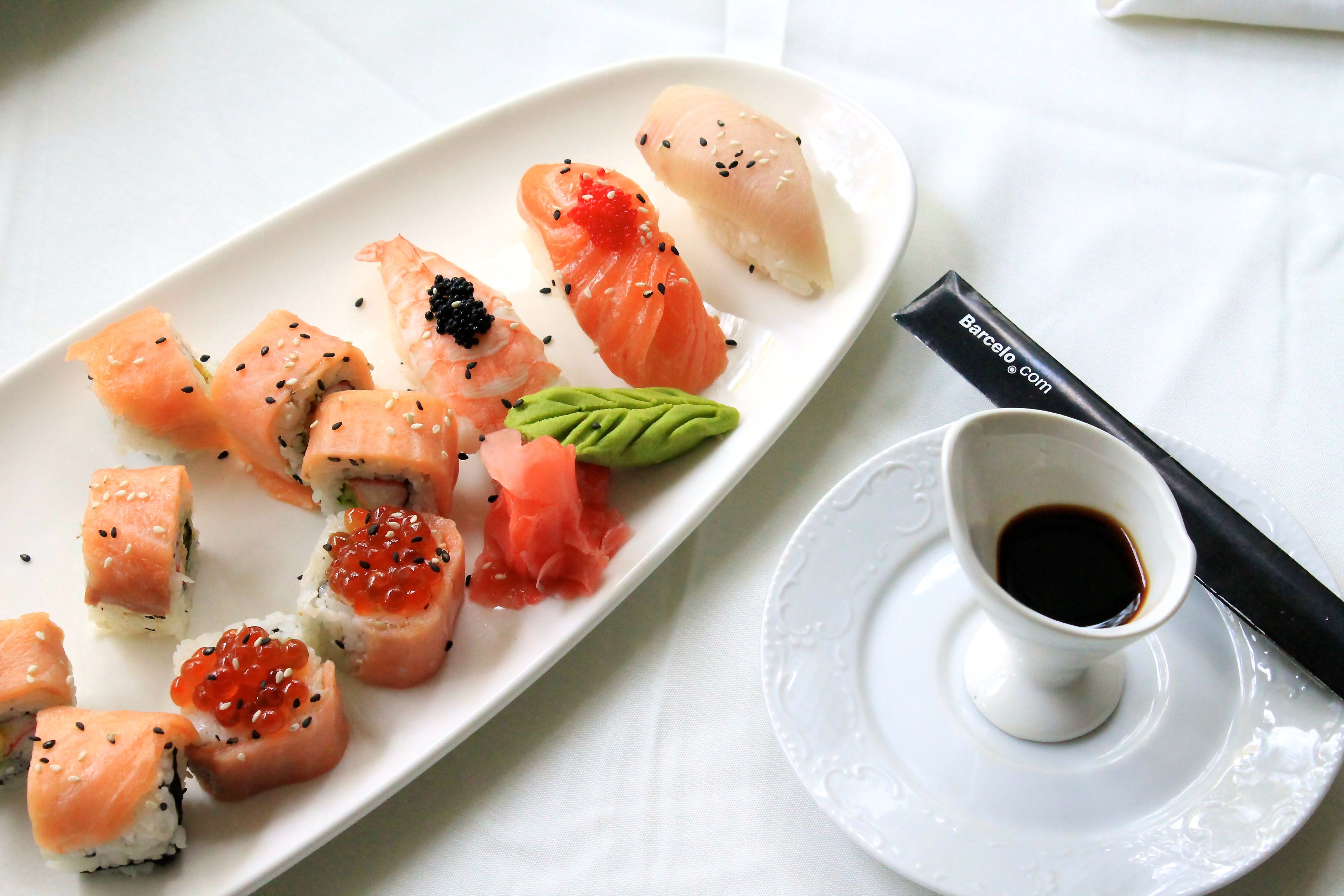 Un piatto di sushi con una piccola tazza di salsa di soia e bacchette su una tovaglia bianca.