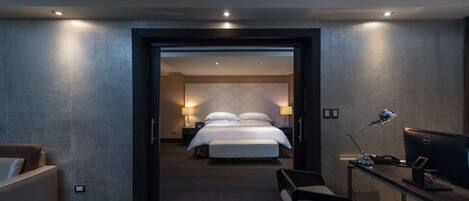 Una habitación de hotel con una cama, mesitas de noche, un escritorio con computadora y una zona de estar.