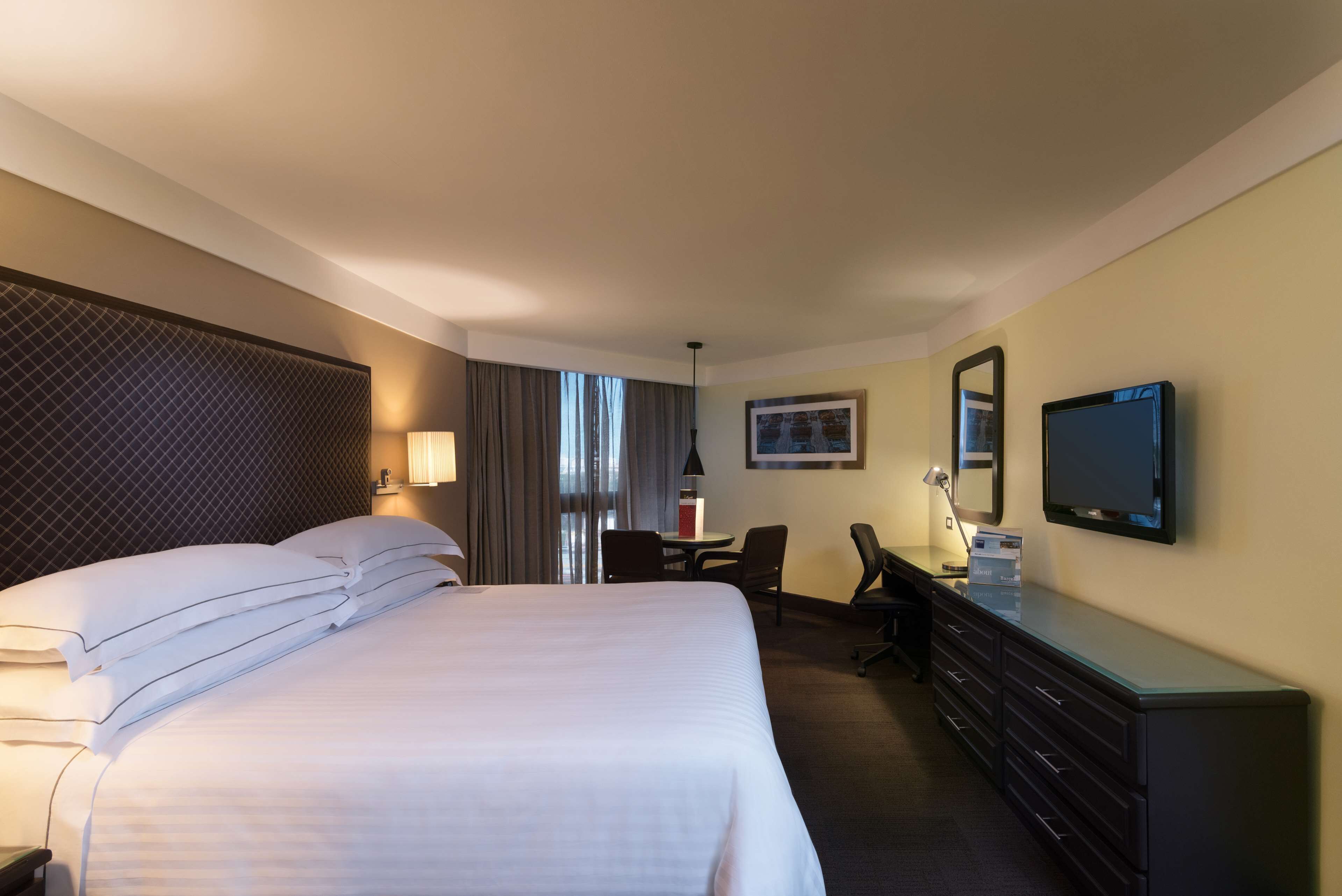 A hotel room with a large bed, a desk, a chair, a television, and a dresser.