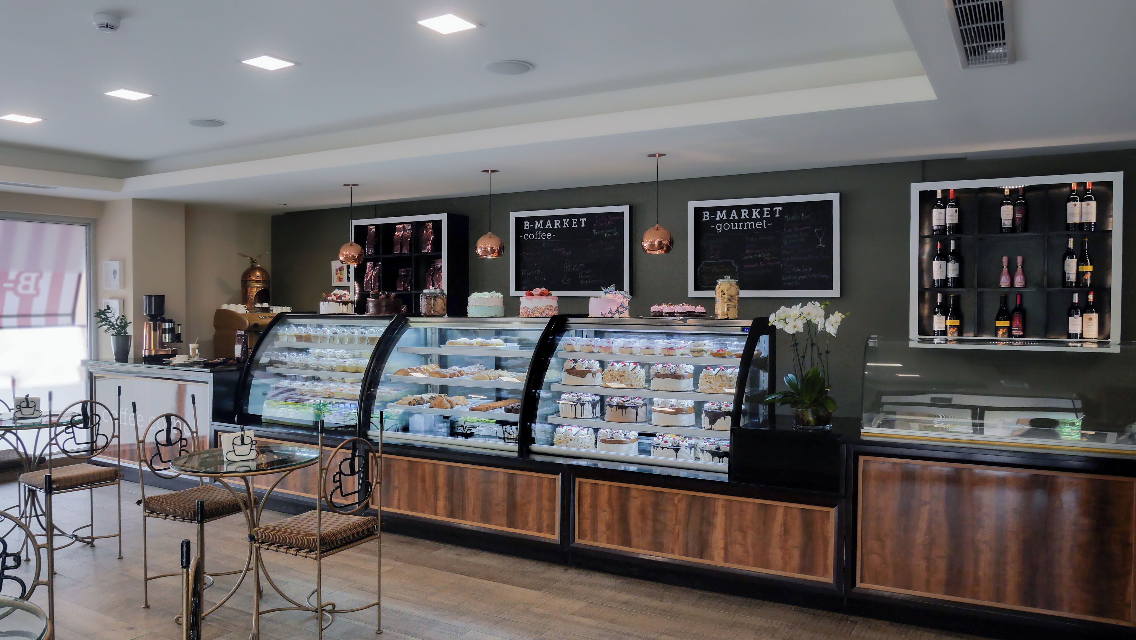 Mostrador de panadería con diversos pasteles y tartas, una estación de café y una exhibición de vinos.