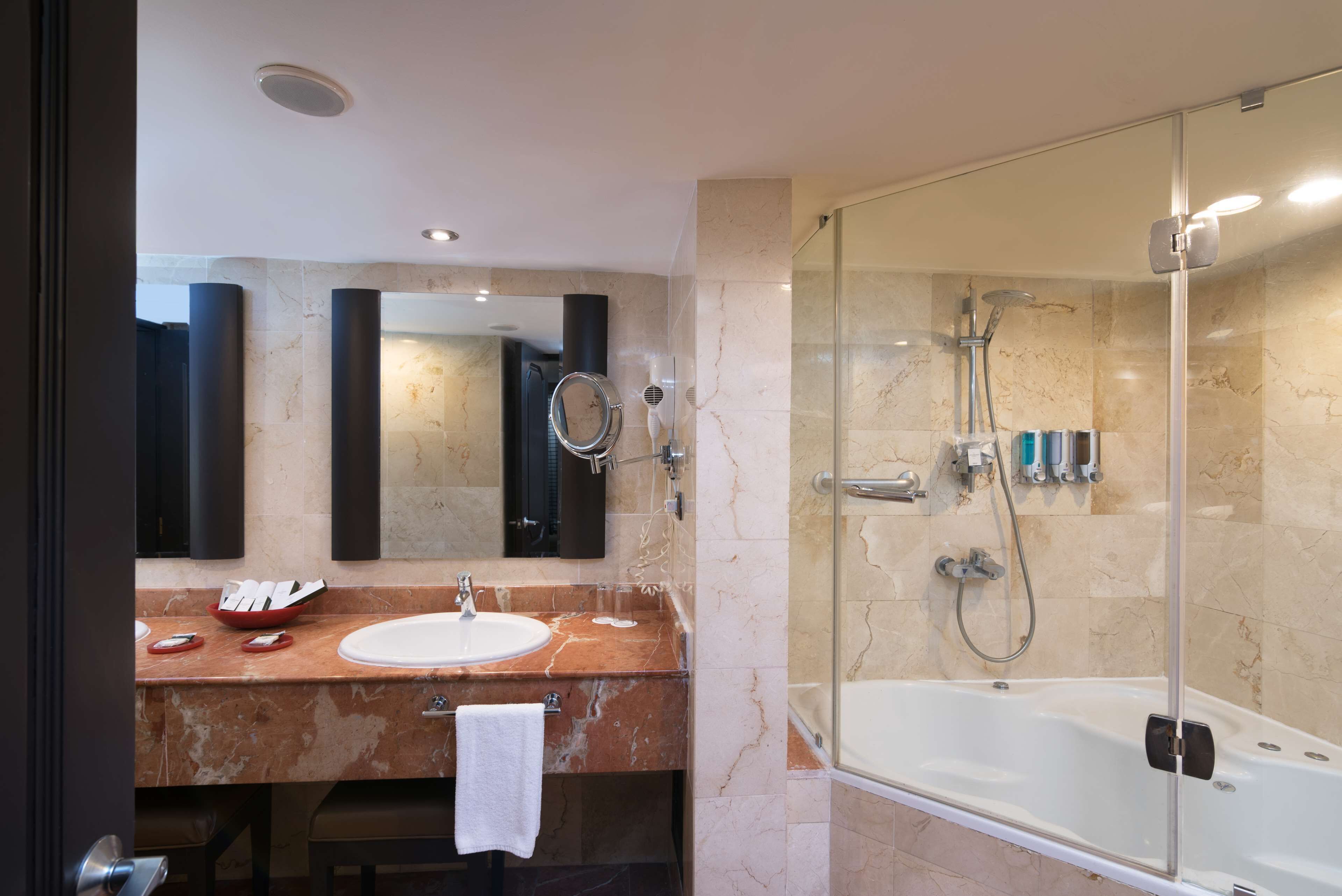 Un baño moderno con lavamanos de mármol, ducha con cerramiento de vidrio y un espejo grande.