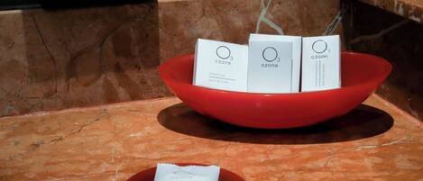 Un tazón rojo que contiene tres cajas blancas etiquetadas 'ozone' con texto en varios idiomas, y un paquete blanco más pequeño sobre un plato rojo a su lado.