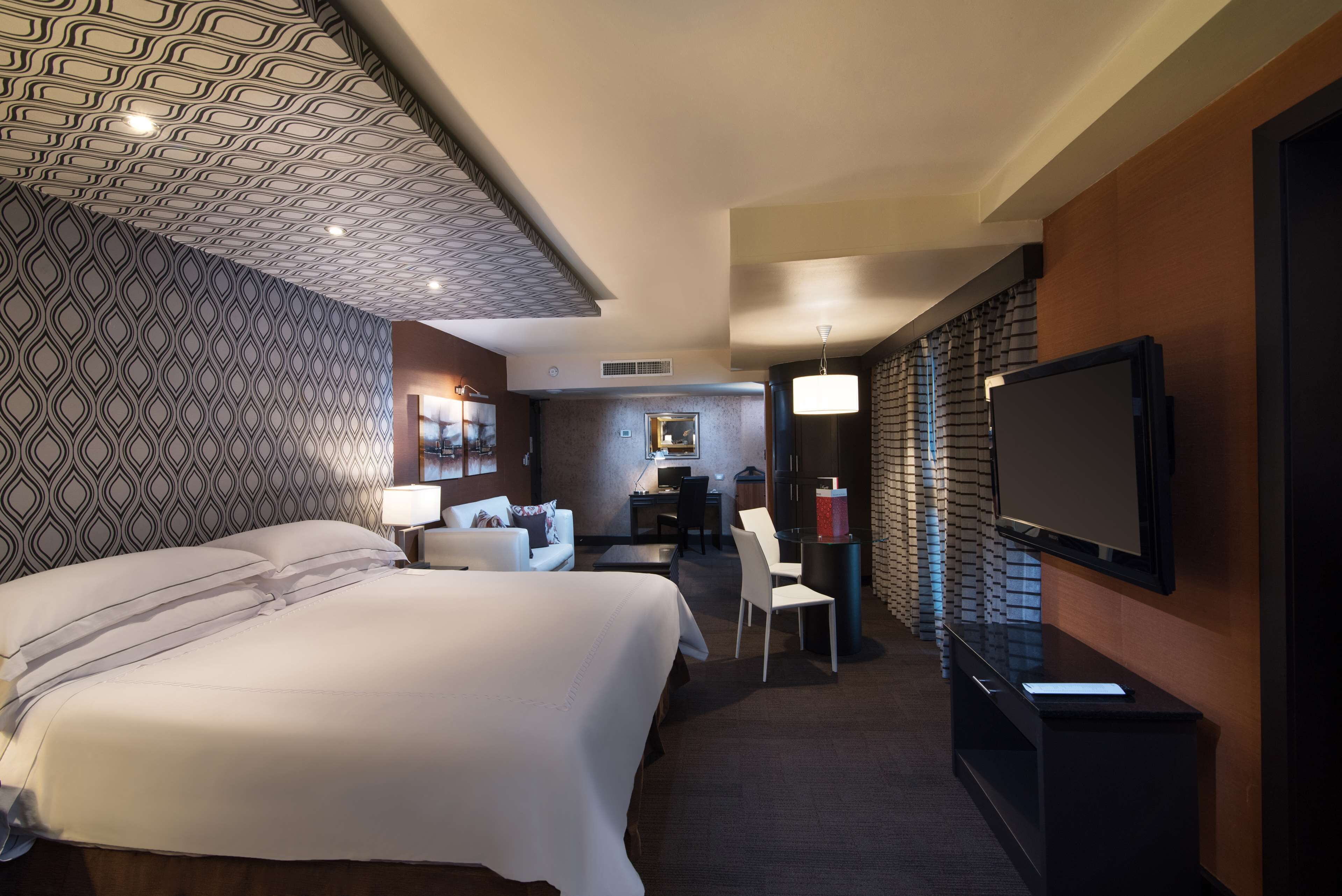 Habitación de hotel con una cama grande, un escritorio, una silla, un televisor y una pared con diseño.