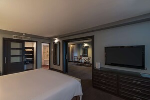 Habitación de hotel con cama, televisor, armario y baño visible a través de una puerta abierta.