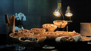 Un tavolo con diversi tipi di pane e dolci, un vaso con fiori bianchi e una lampada.