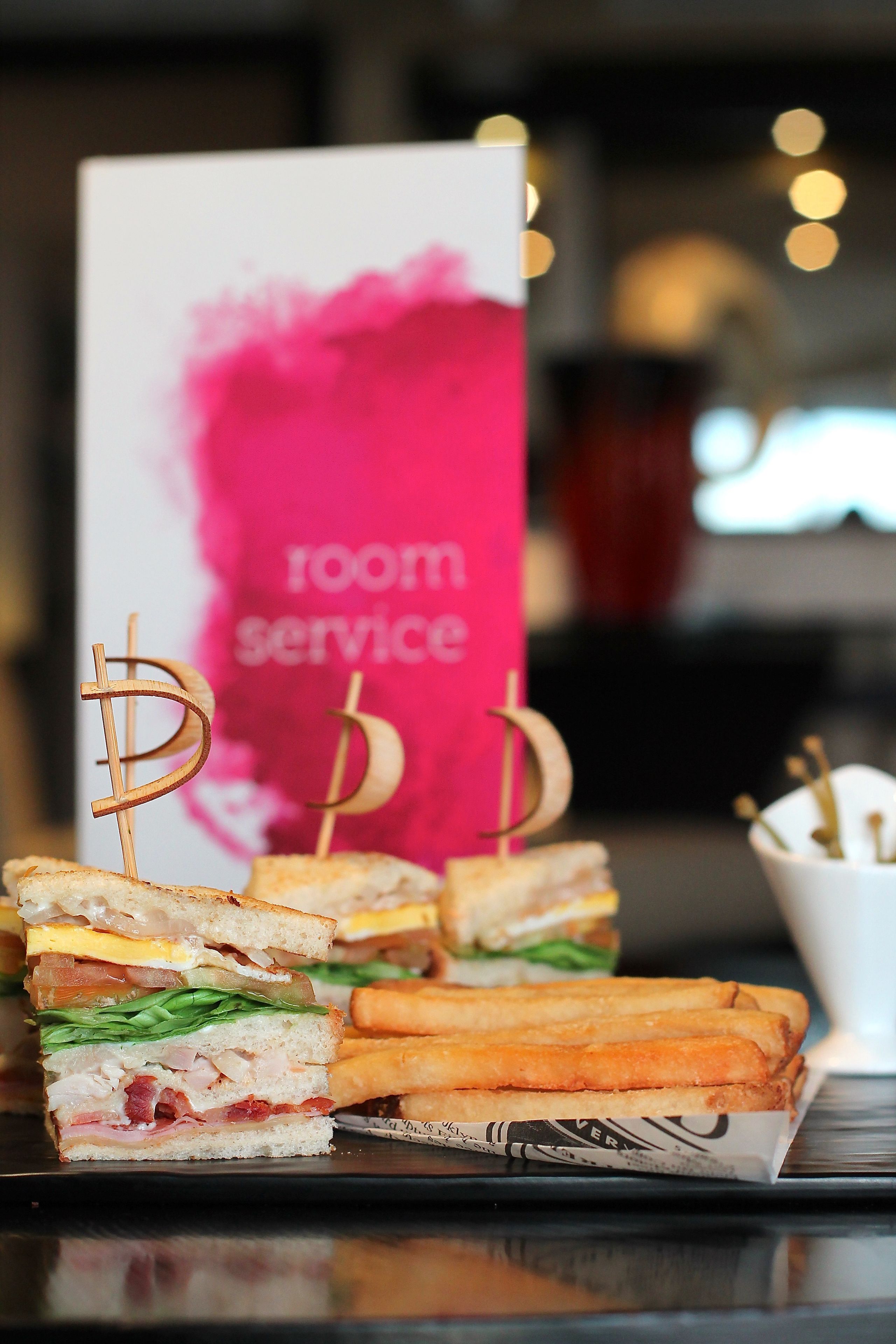 A sandwich with toothpicks shaped like dollar signs, a sign with "room service" written on it, and a cup with toothpicks.