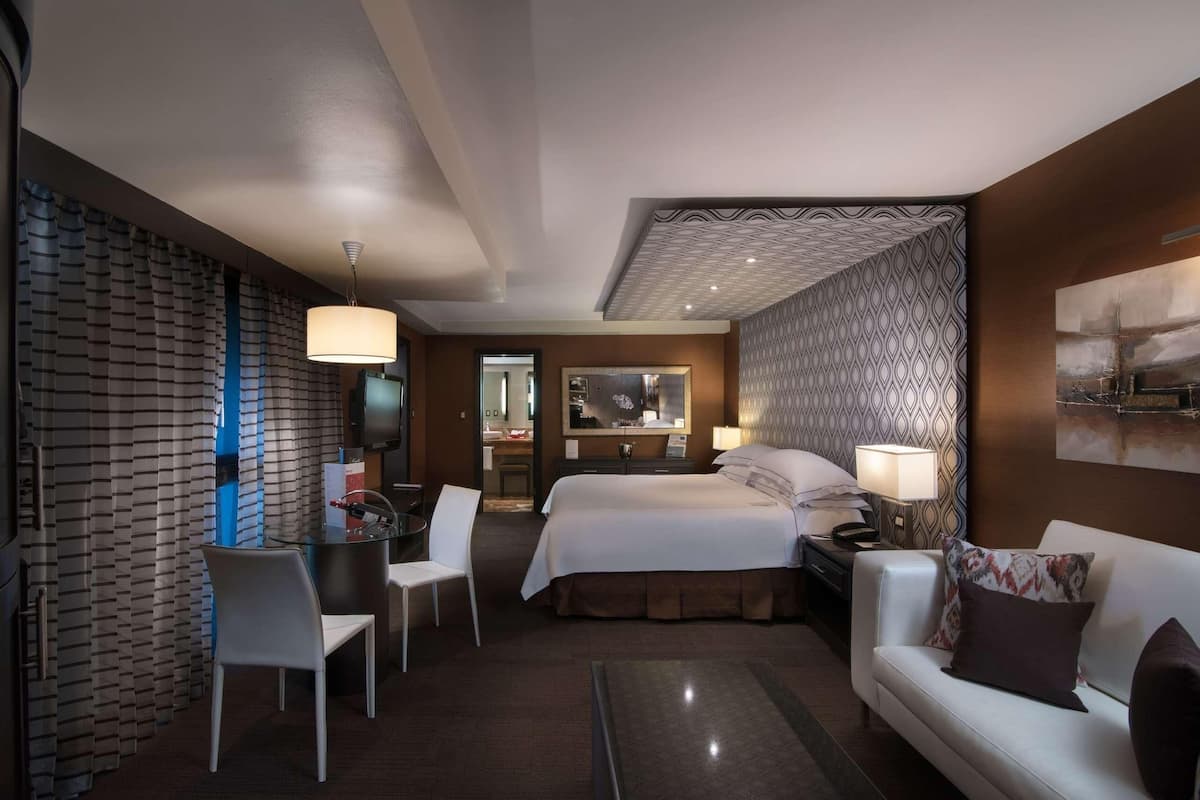 A hotel room with a bed, a desk, a chair, a sofa, and a TV.