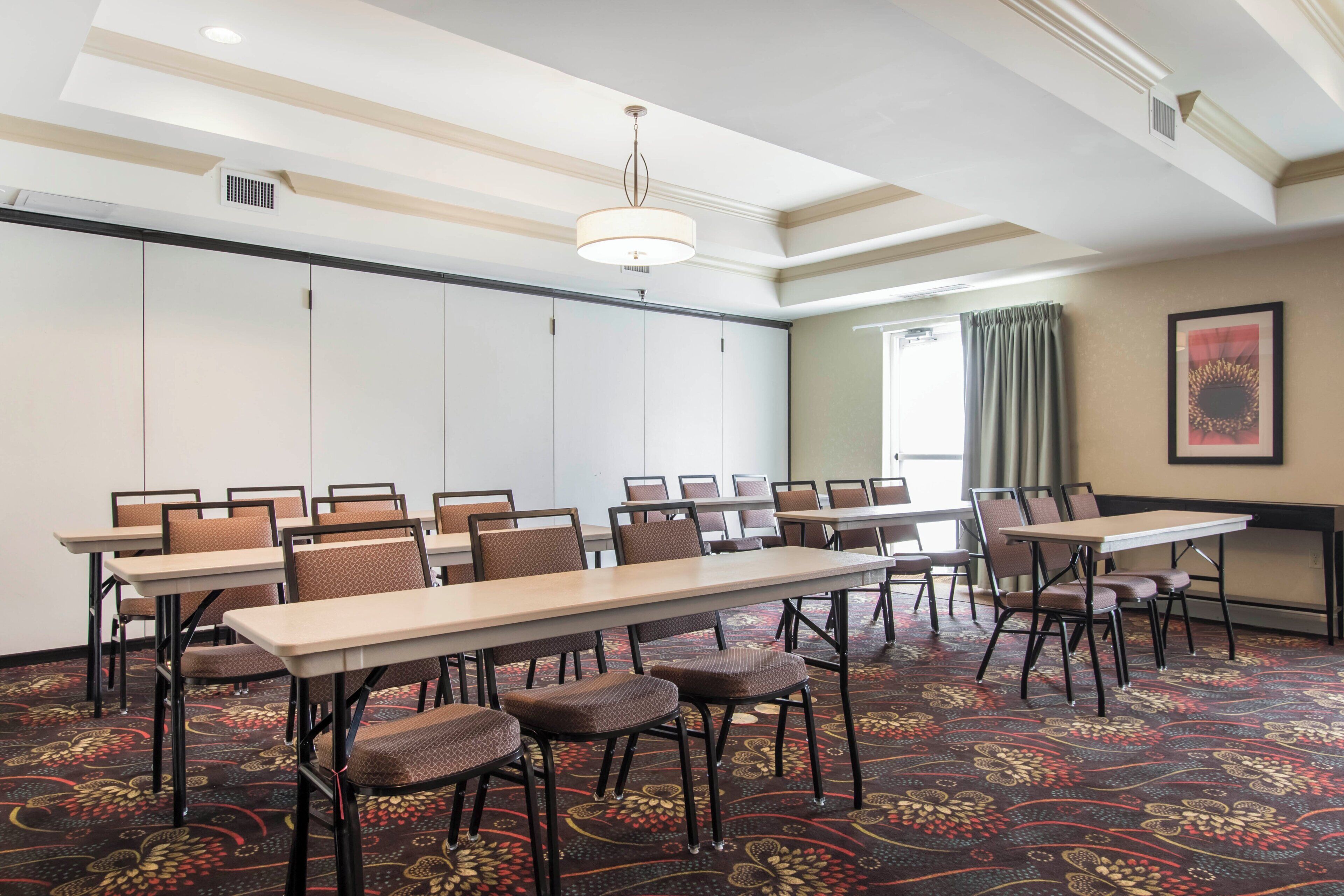 A conference room with a long table, chairs, patterned carpet, and a ceiling light fixture.